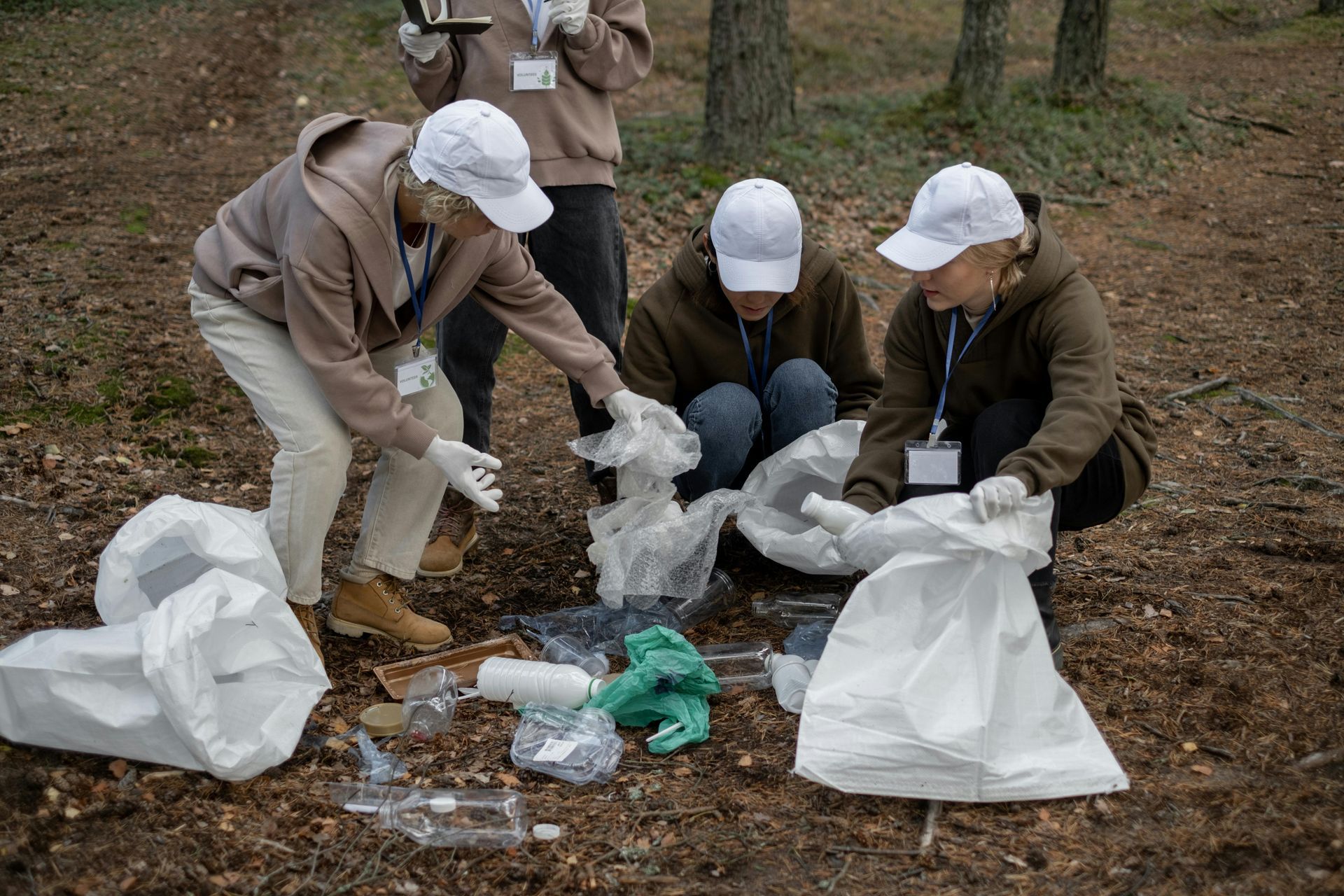 People in white hats and gloves cleaning up trash in a wooded area.