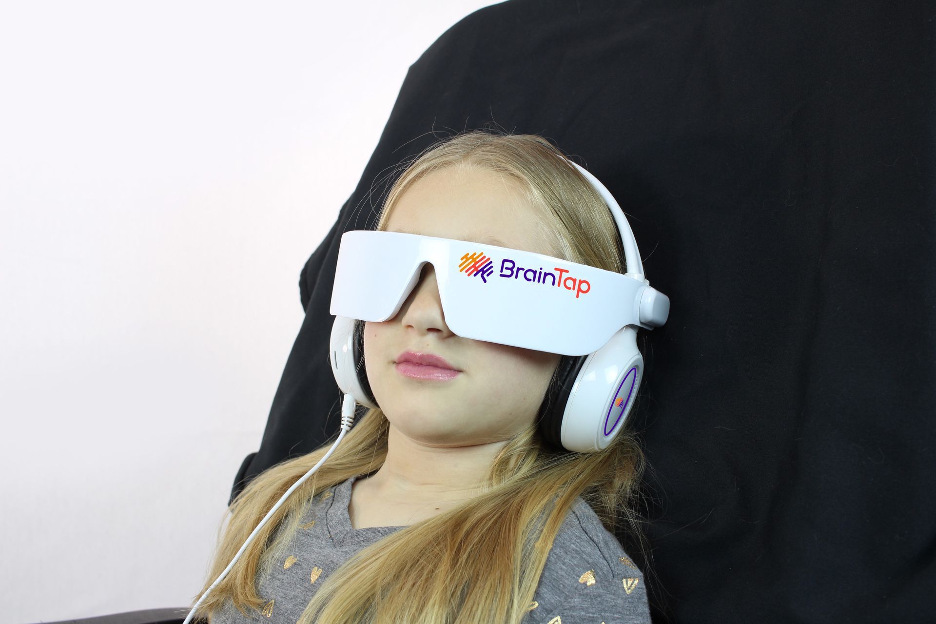 A young girl wearing headphones and sunglasses is sitting in a chair.
