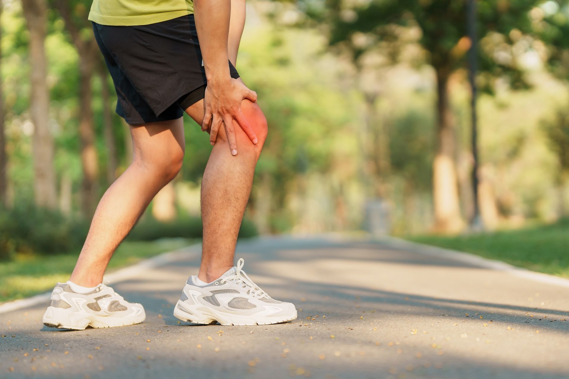 a man is holding his knee in pain while standing on a road .