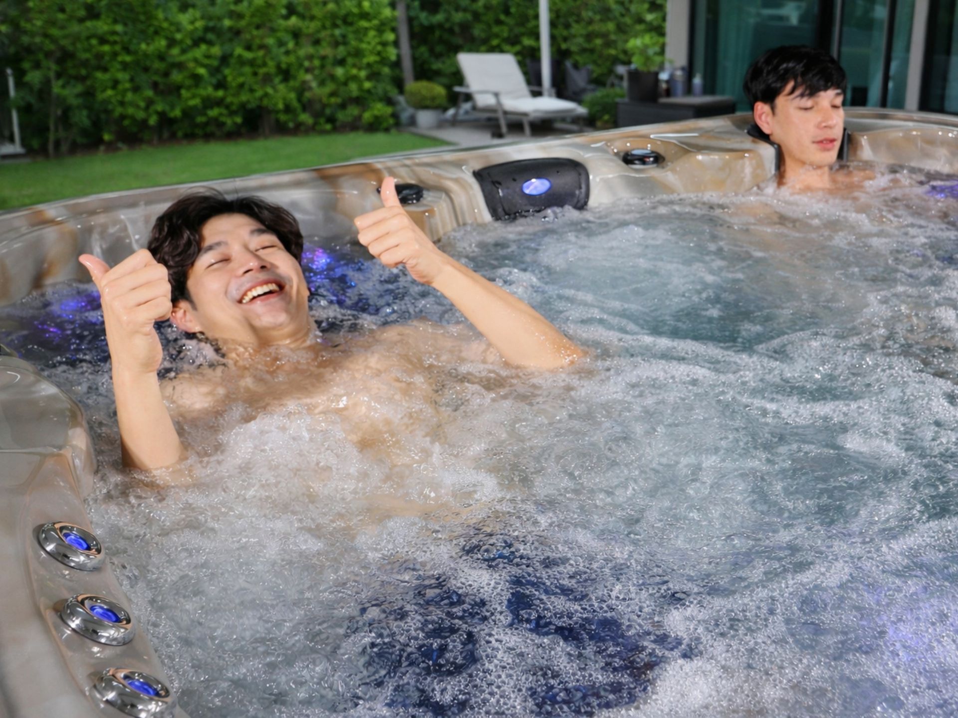 ผู้ใช้งานกำลังแช่อ่างน้ำร้อนกลางแจ้งรุ่นพรีเมียม ระบบเจ็ตนวดทำงานเต็มที่ เกิดฟองน้ำทั่วอ่าง พร้อมไฟ LED ใต้น้ำ สร้างบรรยากาศผ่อนคลายในสวนบ้าน