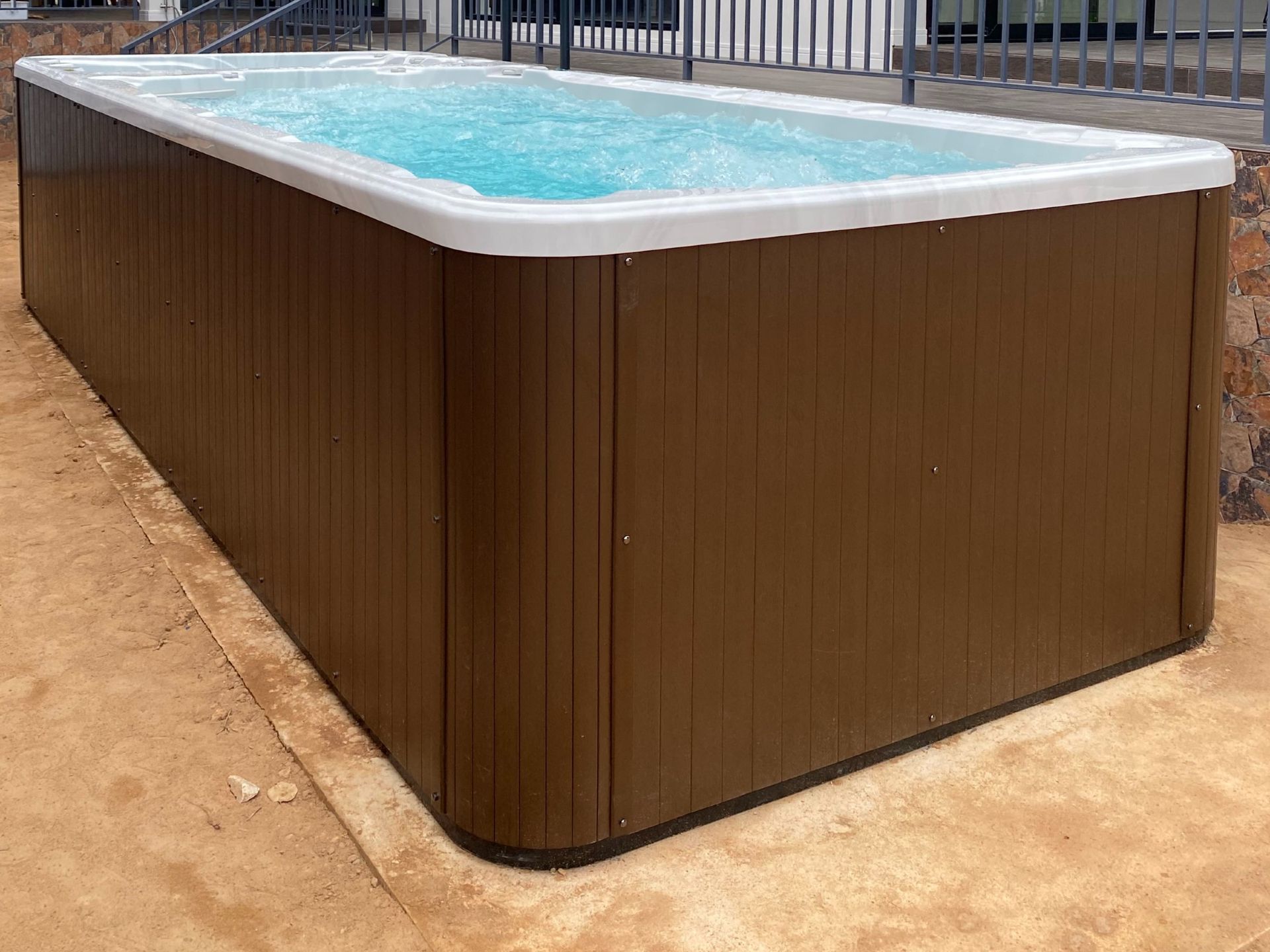 สระว่ายน้ำทวนกระแส รุ่น อาเธนส์ ทู ขนาดเล็ก ติดตั้งพร้อมใช้งาน ตกแต่งด้วยไม้เทียมรอบสระ ช่วยปกป้องโครงสร้างและระบบภายใน เพิ่มความแข็งแรงและยืดอายุการใช้งานของสระว่ายน้ำ