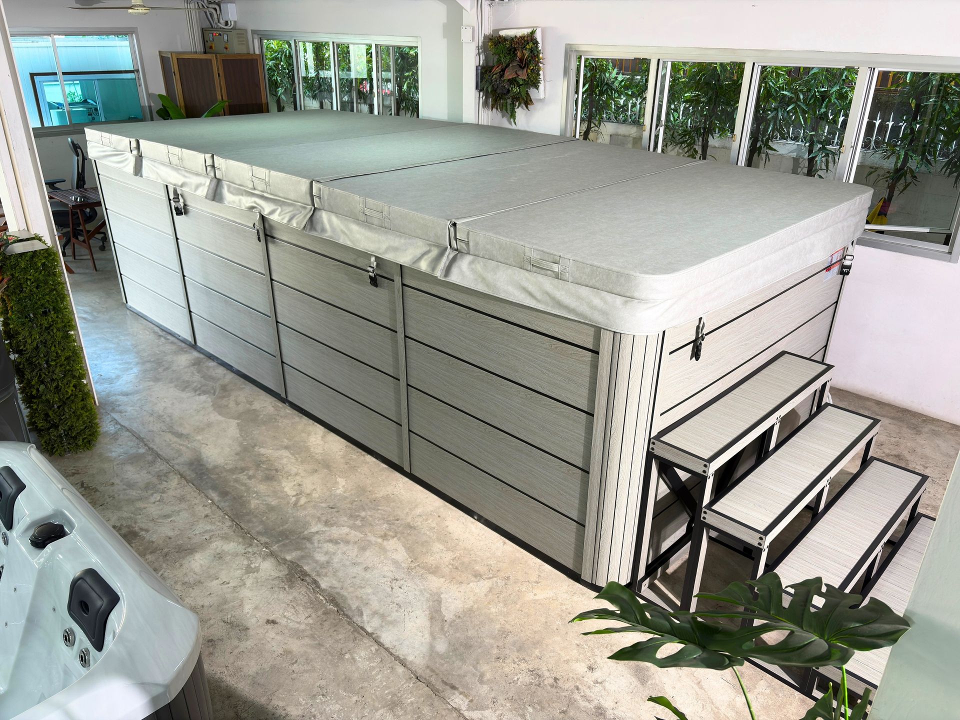 Large swim spa with composite cabinet and insulated hard cover, built on a galvanized steel frame, displayed indoors.