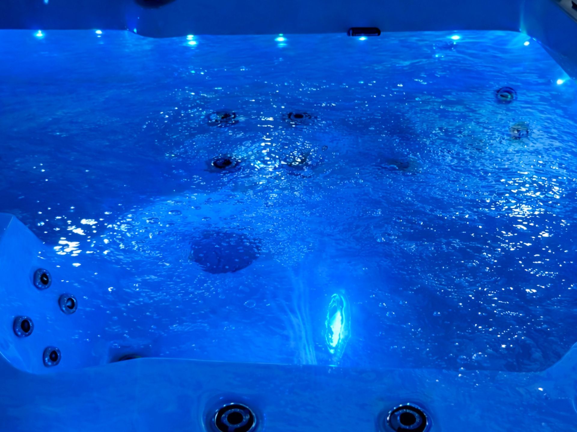 ภาพภายในอ่างน้ำร้อนที่เปิดระบบไฟ LED ใต้น้ำ แสดงแสงสีน้ำเงินส่องสว่างทั่วผิวน้ำ พร้อมฟองอากาศจากระบบเจ็ต ช่วยสร้างบรรยากาศผ่อนคลาย เหมาะสำหรับการใช้งานในช่วงกลางคืน
