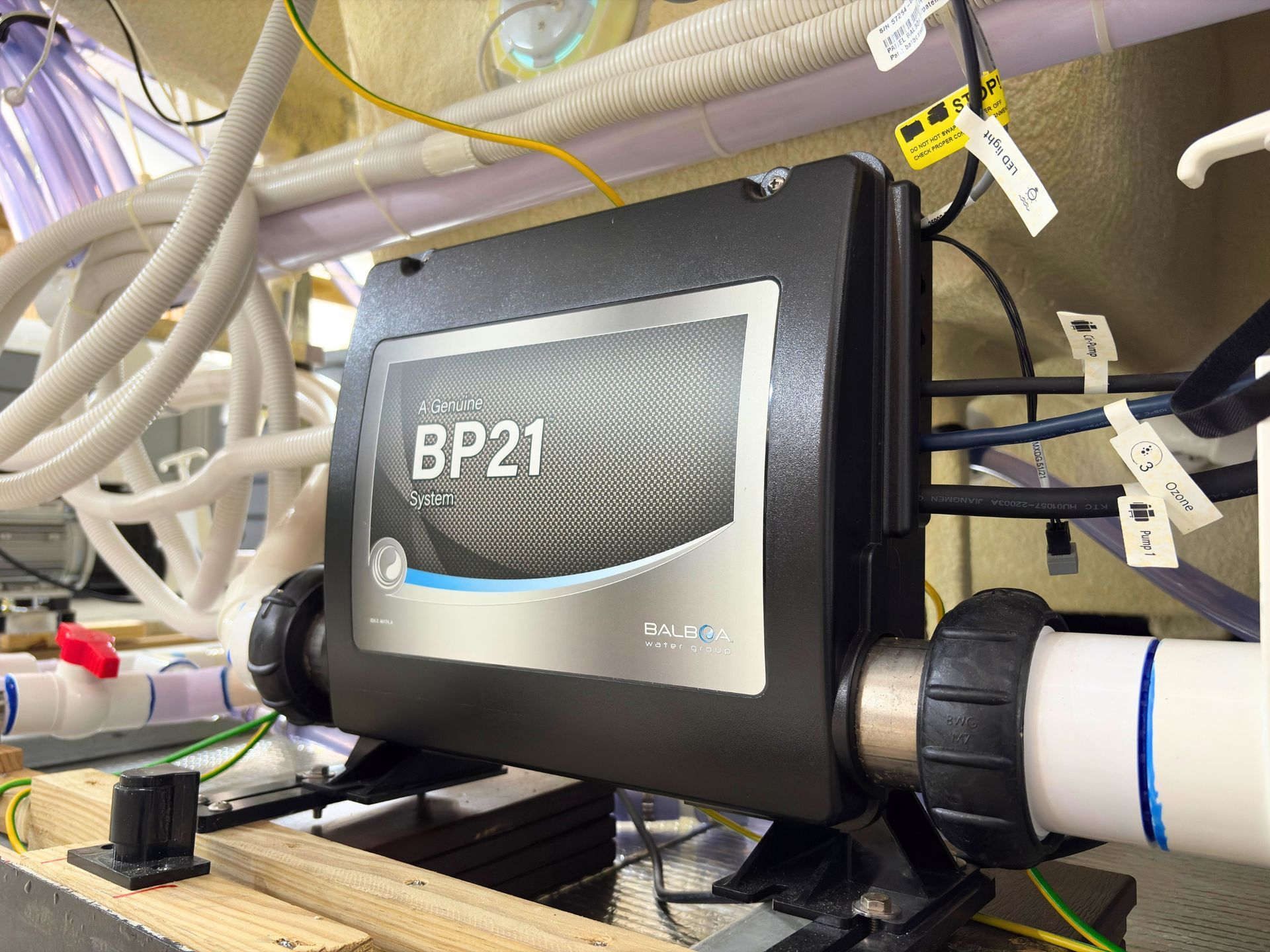 Balboa BP21 spa control unit mounted inside a hot tub cabinet with connected plumbing and electrical cables.