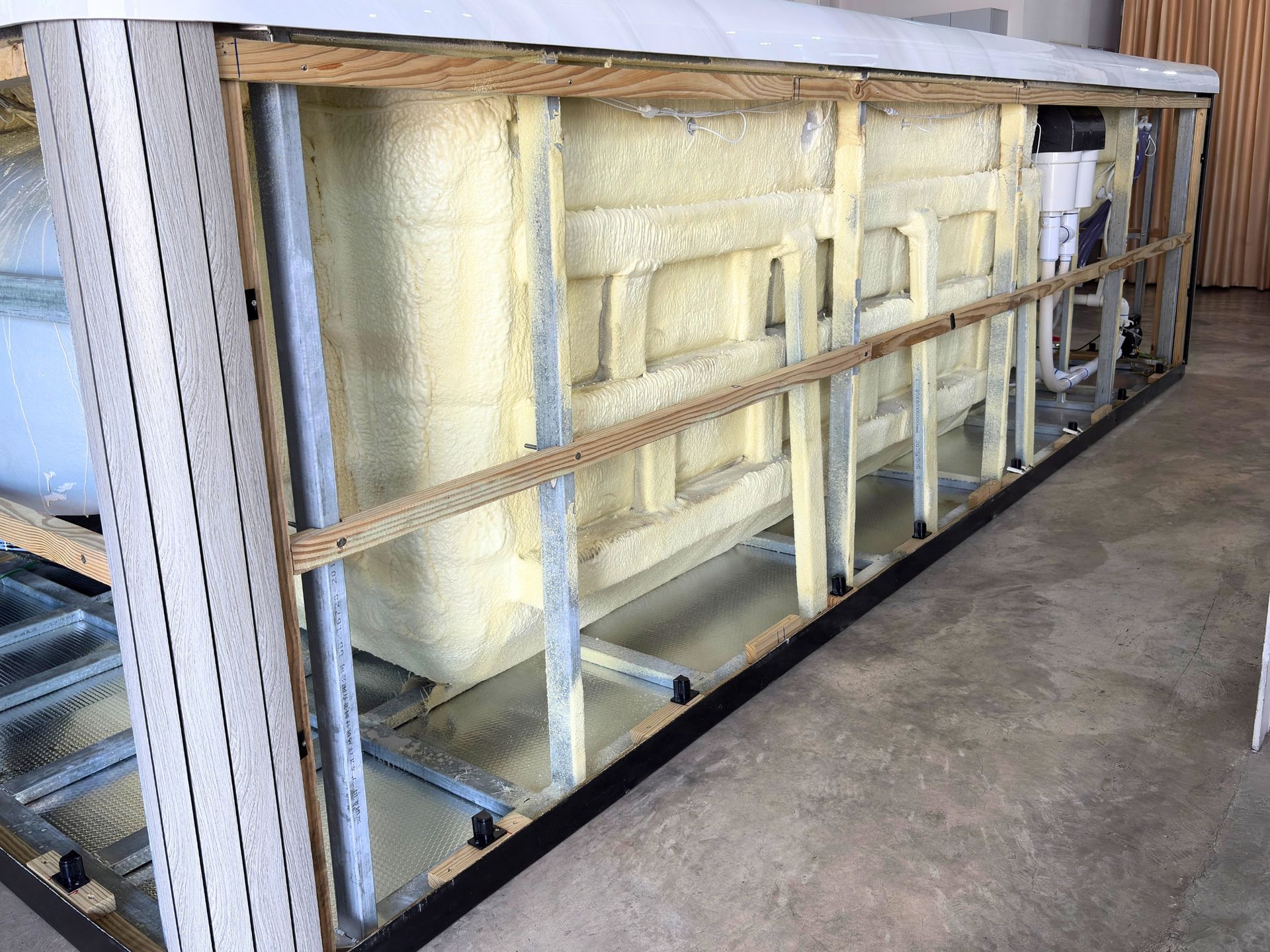 Interior of swim spa showing galvanized steel frame, spray foam insulation, and plumbing structure