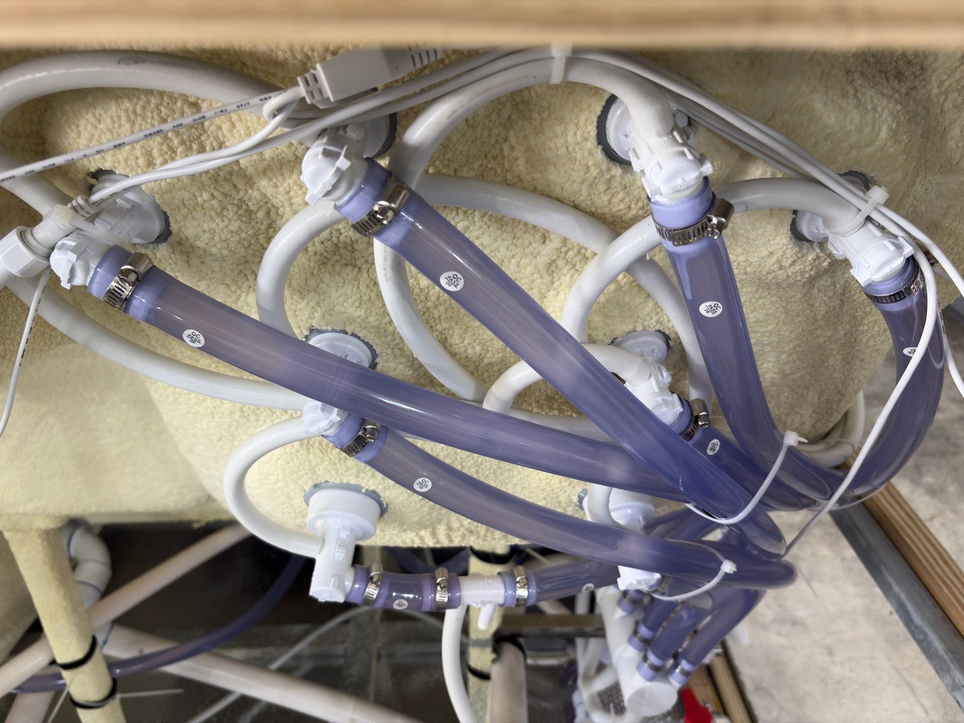 Underside view of hot tub plumbing showing multiple clear and white hoses connected to jet fittings.
