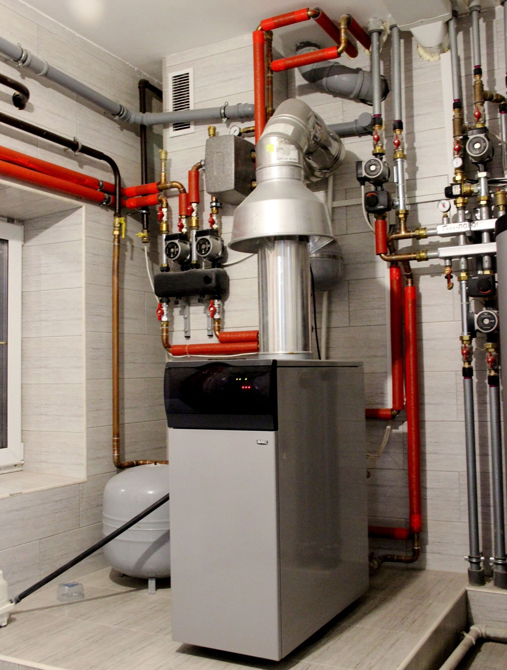 A boiler is sitting in a room surrounded by pipes