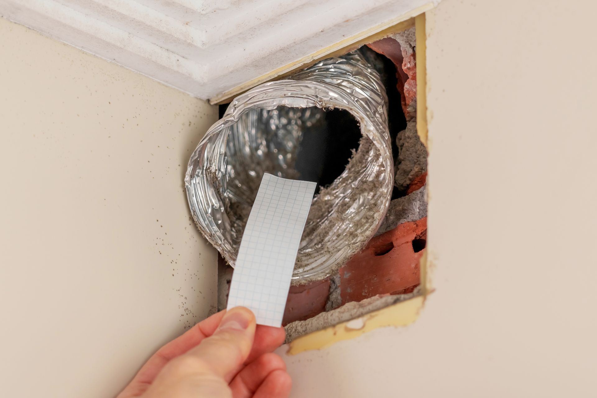 A person is holding a piece of paper in front of a duct.