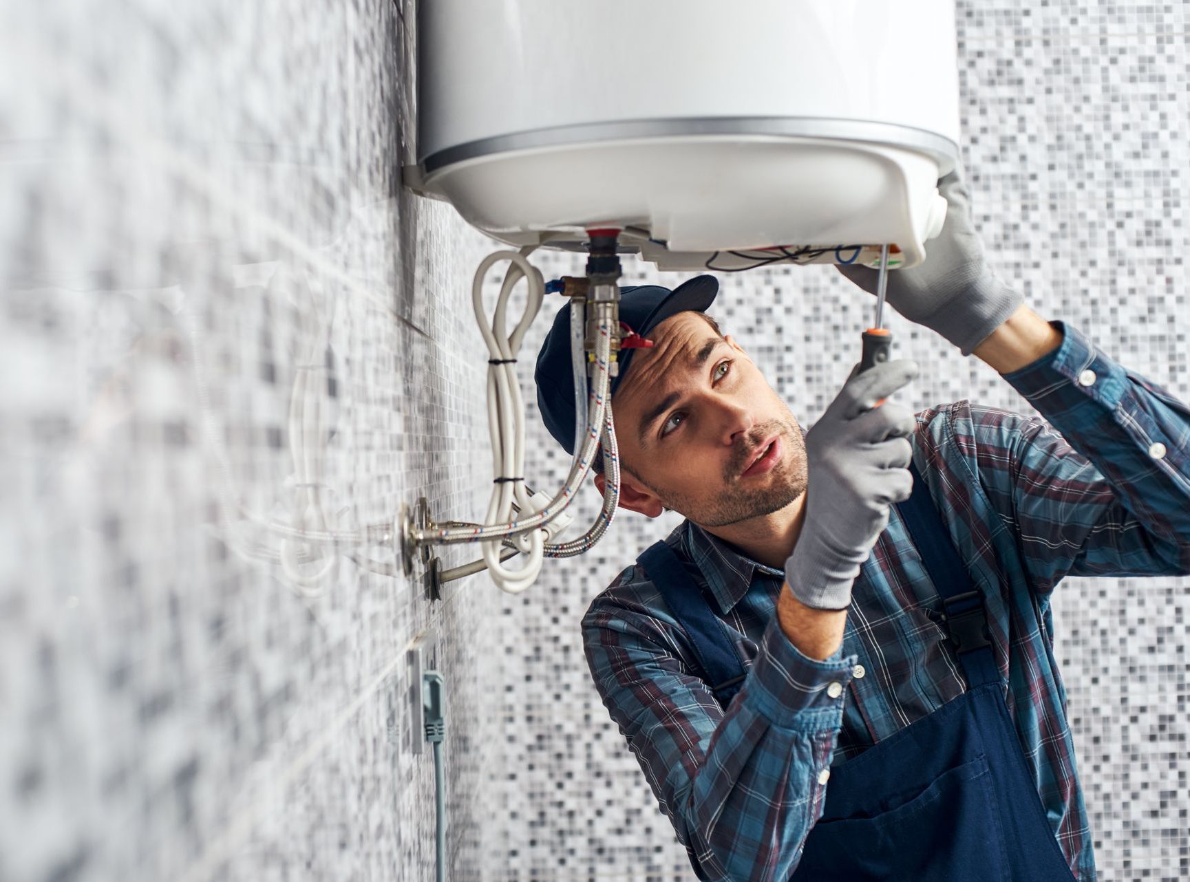 A man is fixing a water heater in a bathroom.