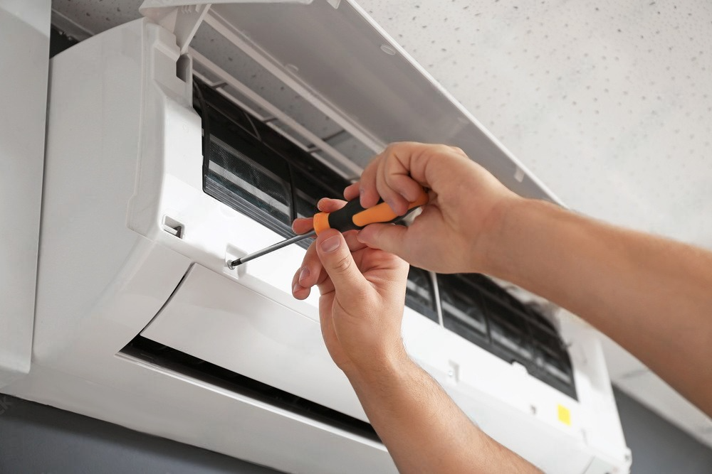 A person is fixing an air conditioner with a screwdriver.