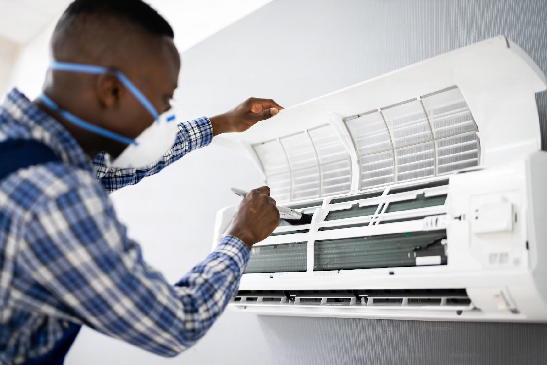 A man wearing a mask is working on an air conditioner.