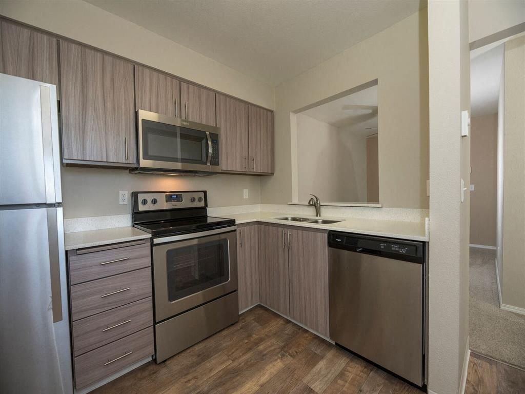 Kitchen in an apartment with stainless steel appliances, wood-tone cabinets, and a pass-through to the living area.