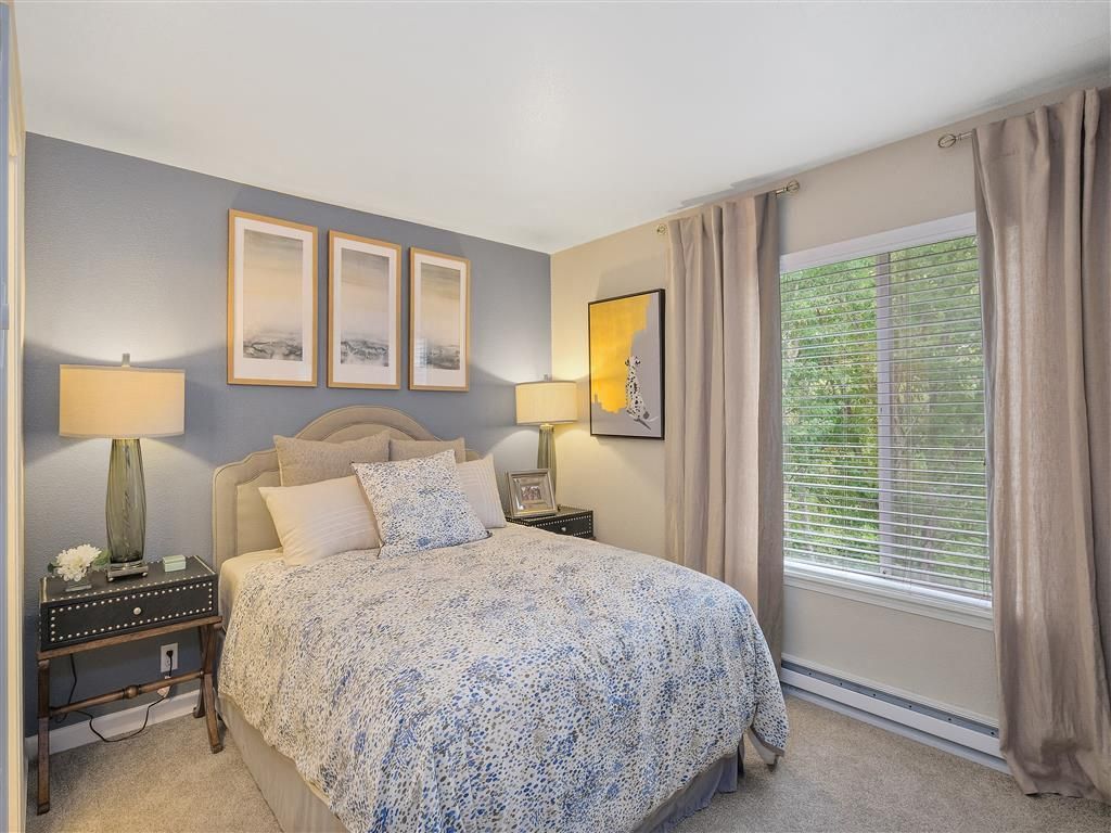 Bedroom with blue accent wall, queen bed with patterned quilt, two nightstands, and a large window with blinds.