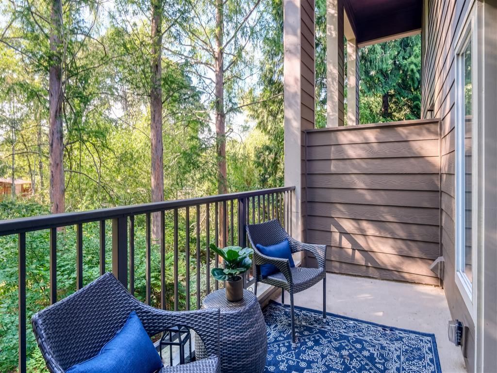 Balcony with two wicker chairs, a small table, blue cushions, and a patterned rug overlooking trees.