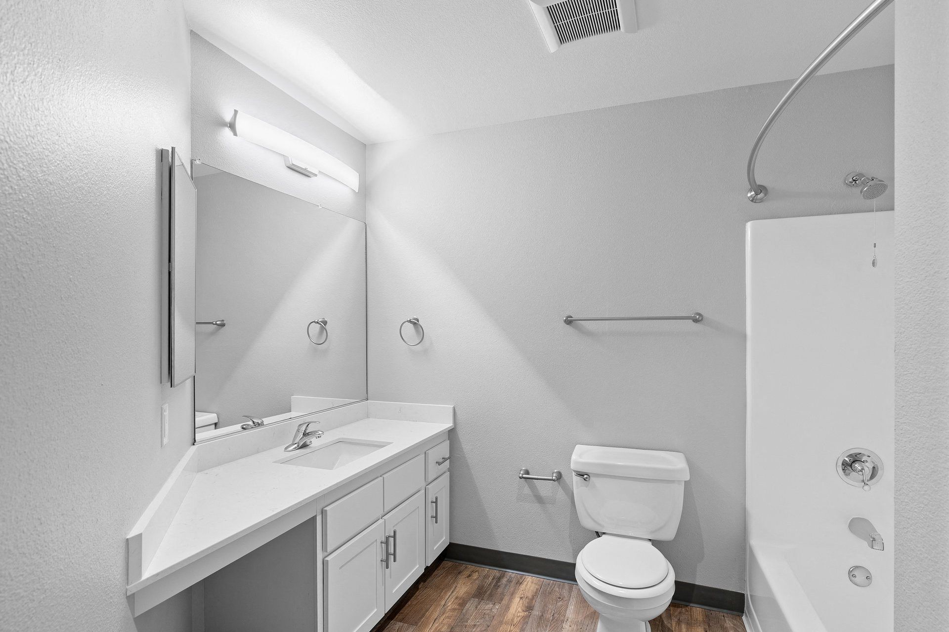 Bathroom in an apartment unit with a long vanity, sink, mirror, toilet, and shower/tub.