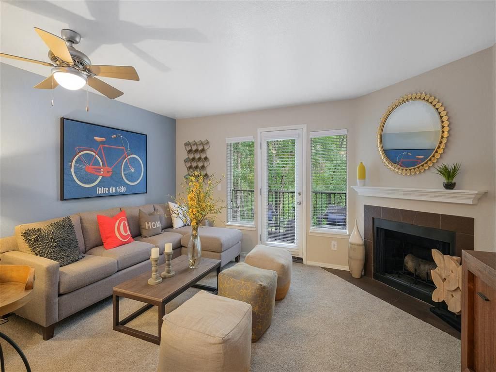 Living room in an apartment with a grey sectional sofa, coffee table, fireplace, and large windows.