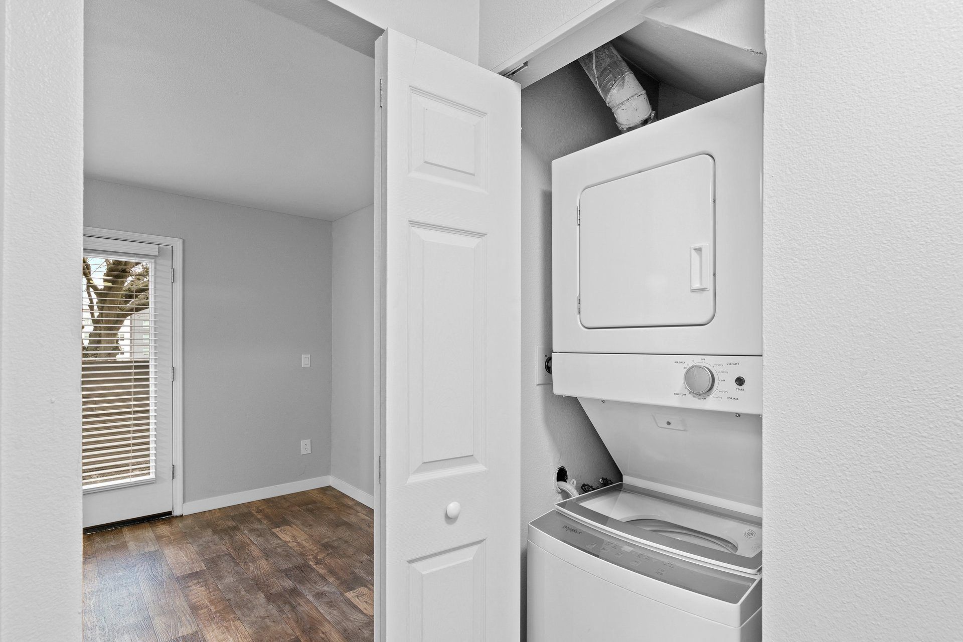 Laundry closet with a stacked washer and dryer beside an interior door; wood flooring visible.