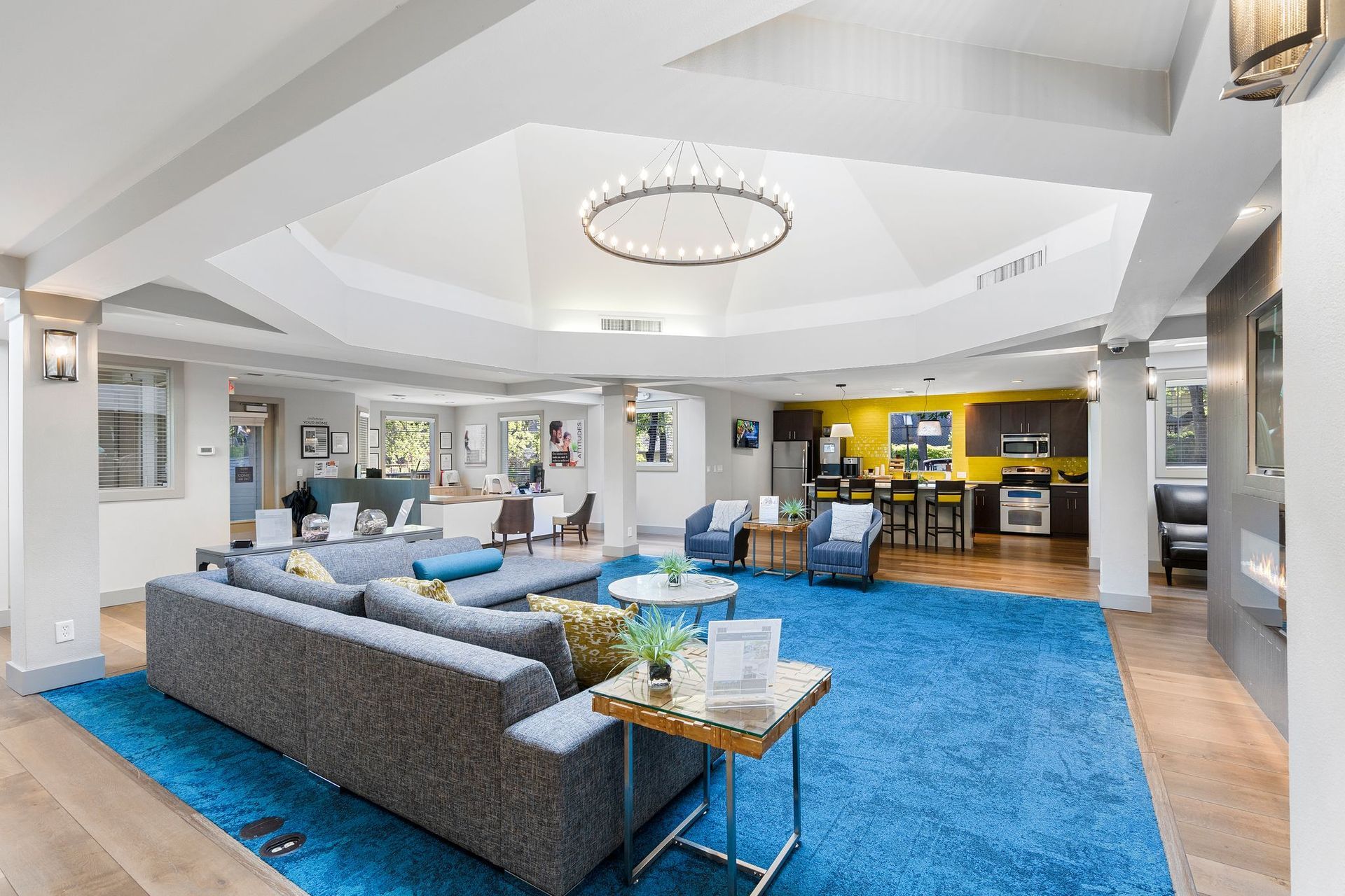Interior of a modern community lounge with a gray sectional, blue rug, and reception area.