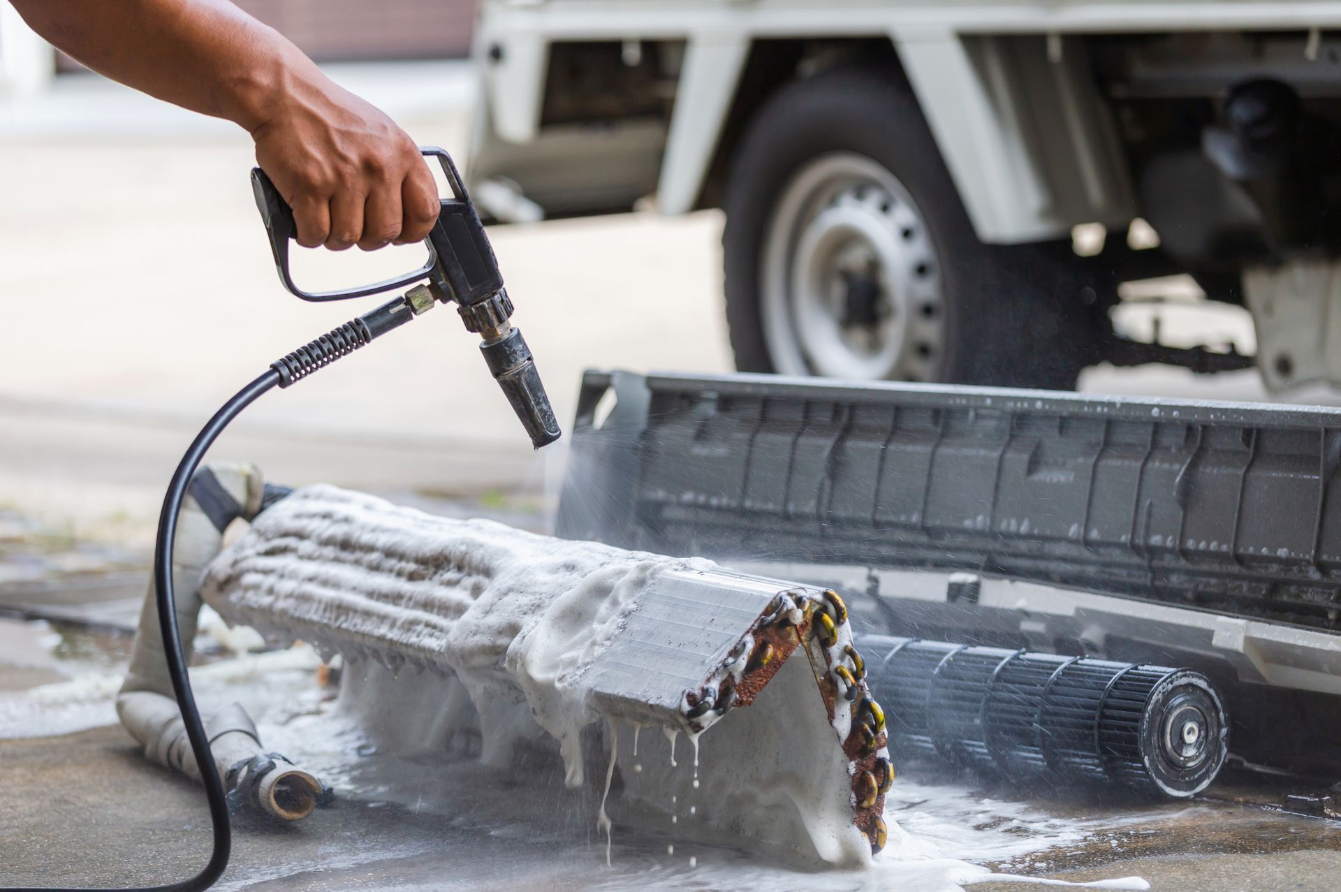 A person is cleaning an air conditioner with a high pressure washer.