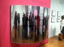 A group of people are standing in front of a mirror in a museum.