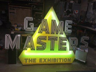A neon sign for the game masters exhibition is lit up in a room.
