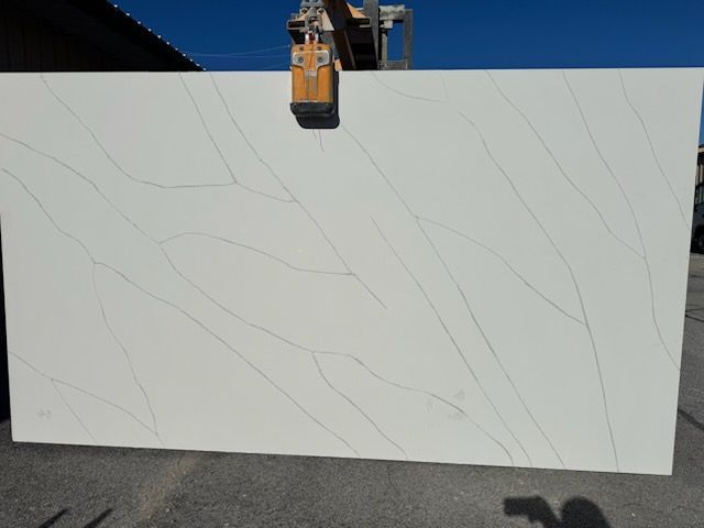 A large white slab of granite is being lifted by a crane.