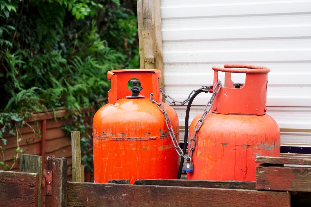 Two Orange Gas Cylinders Beside a Wooden Fence in a Garden — Kuranda Gas & Supplies In Port Douglas, QLD