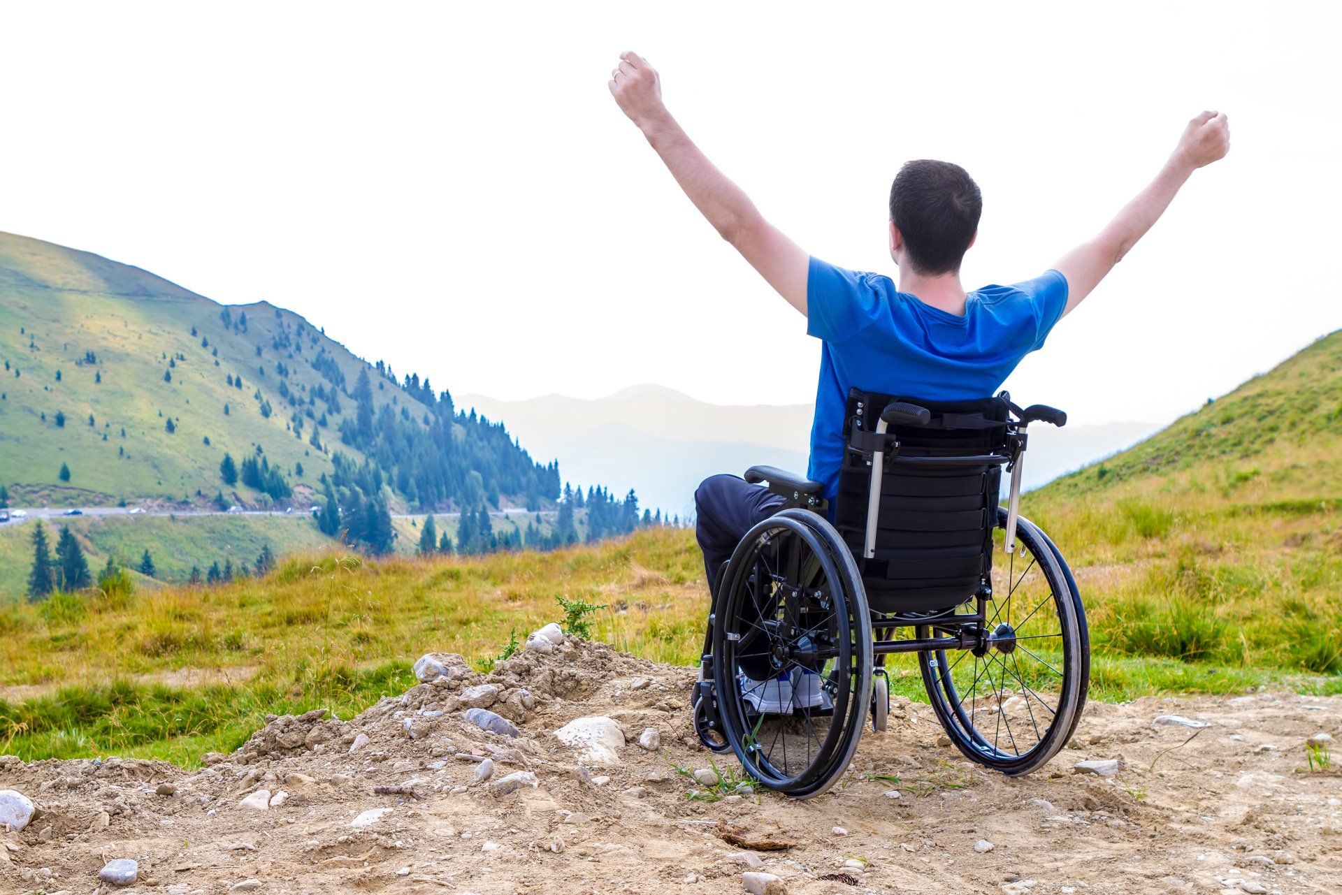 A man in a wheelchair is sitting on top of a hill with his arms outstretched.