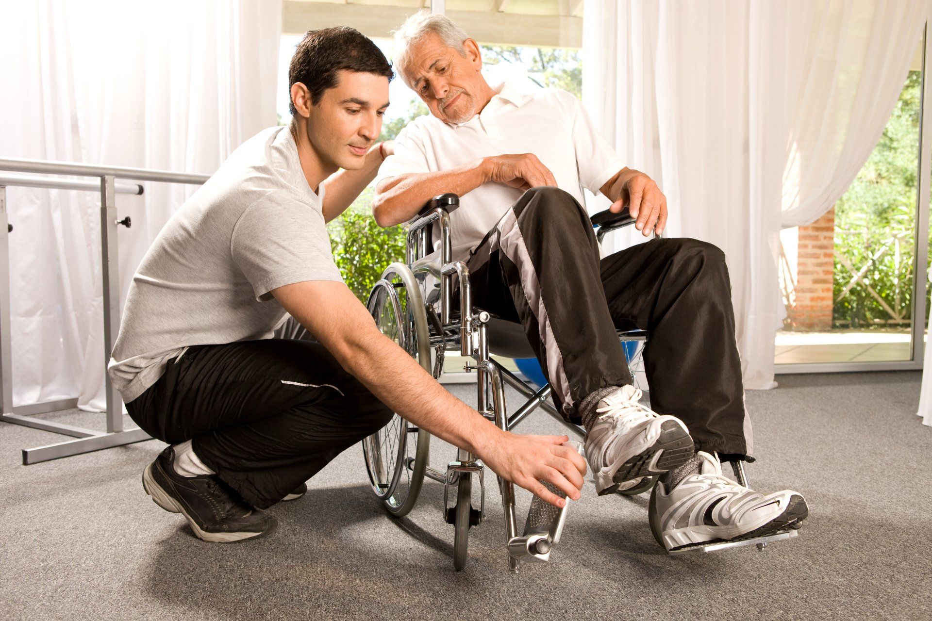 A man is helping an older man in a wheelchair.