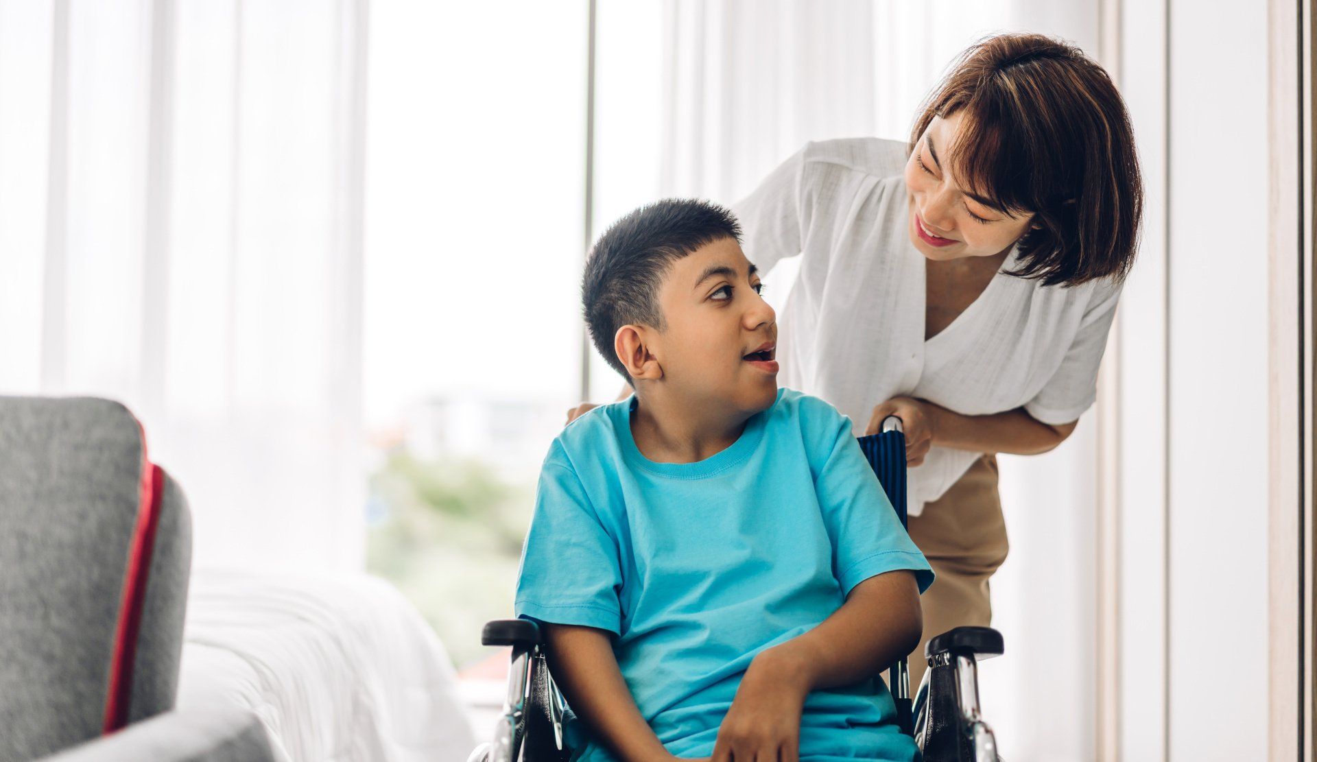 A woman is standing next to a boy in a wheelchair.