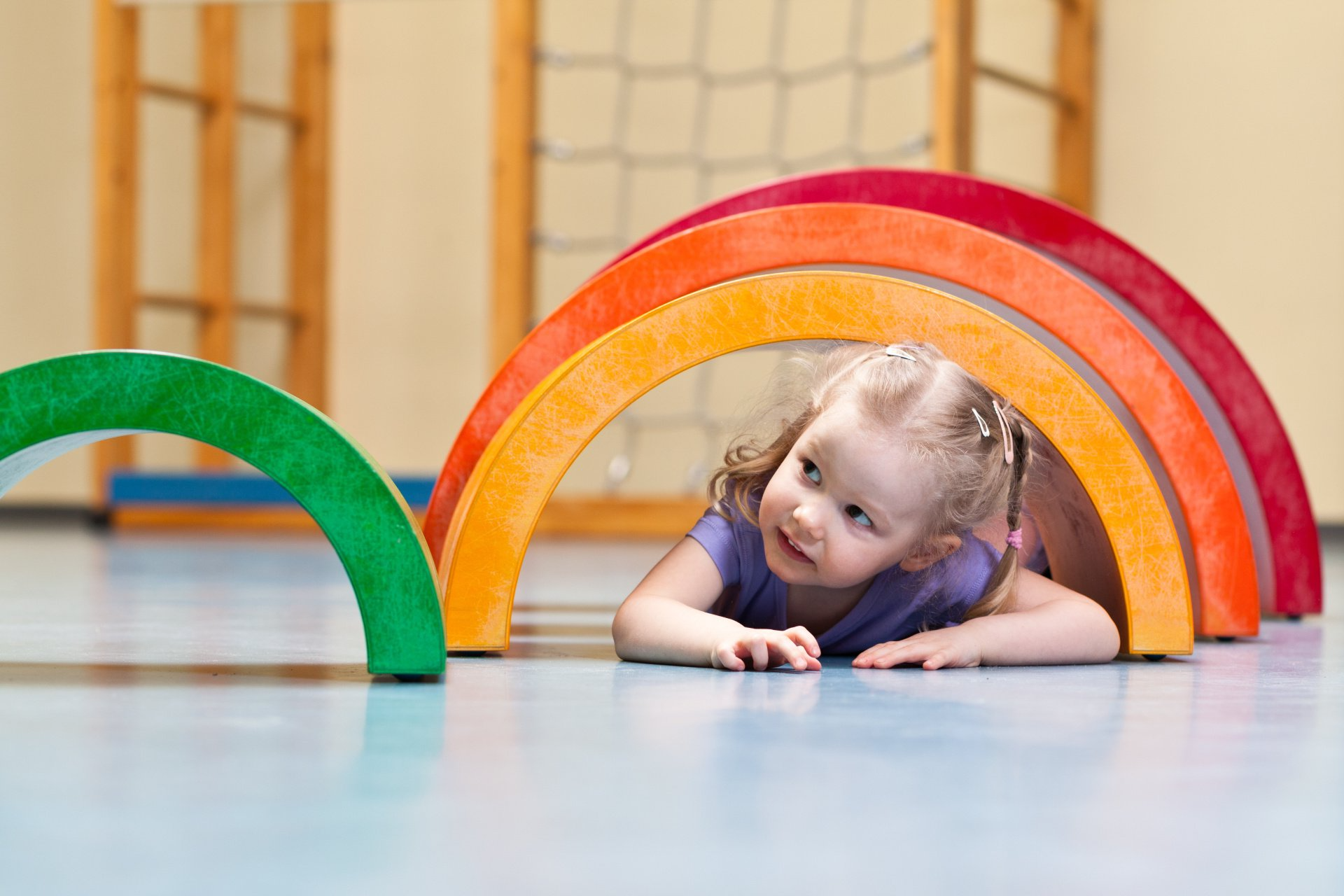 A little girl is crawling through a wooden rainbow.