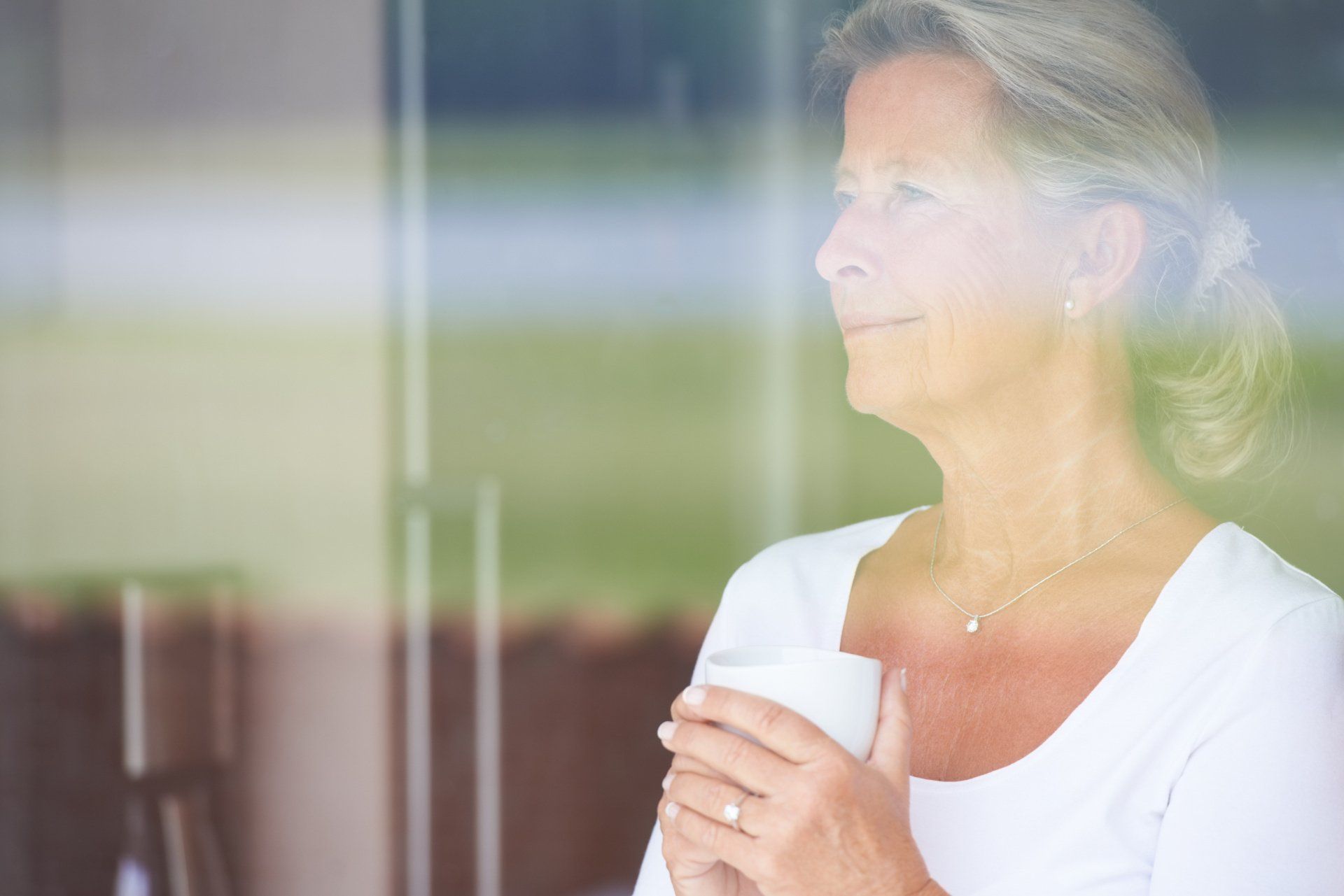 A woman is holding a cup of coffee and looking out of a window.