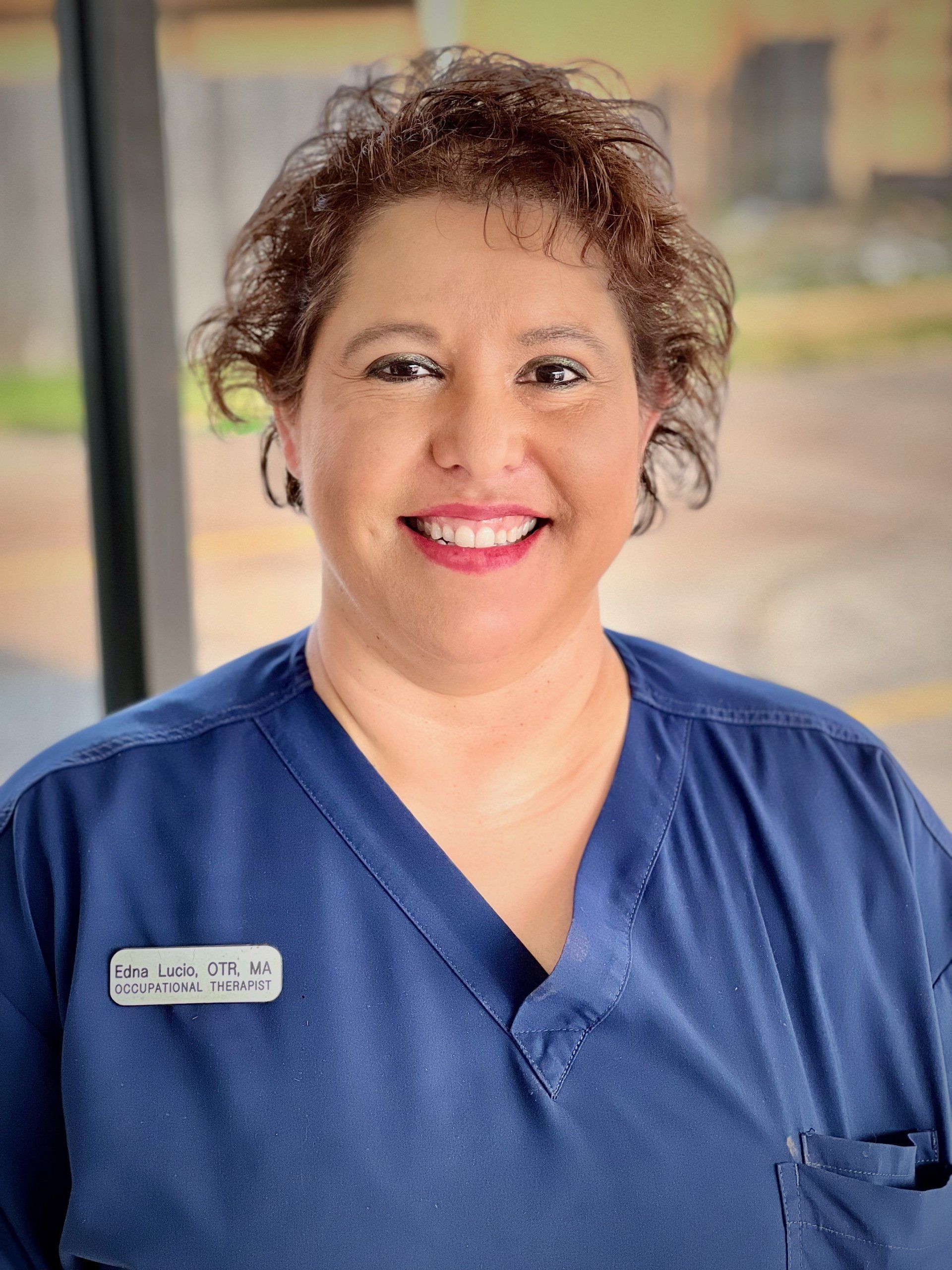 A woman wearing a blue scrub top is smiling for the camera.