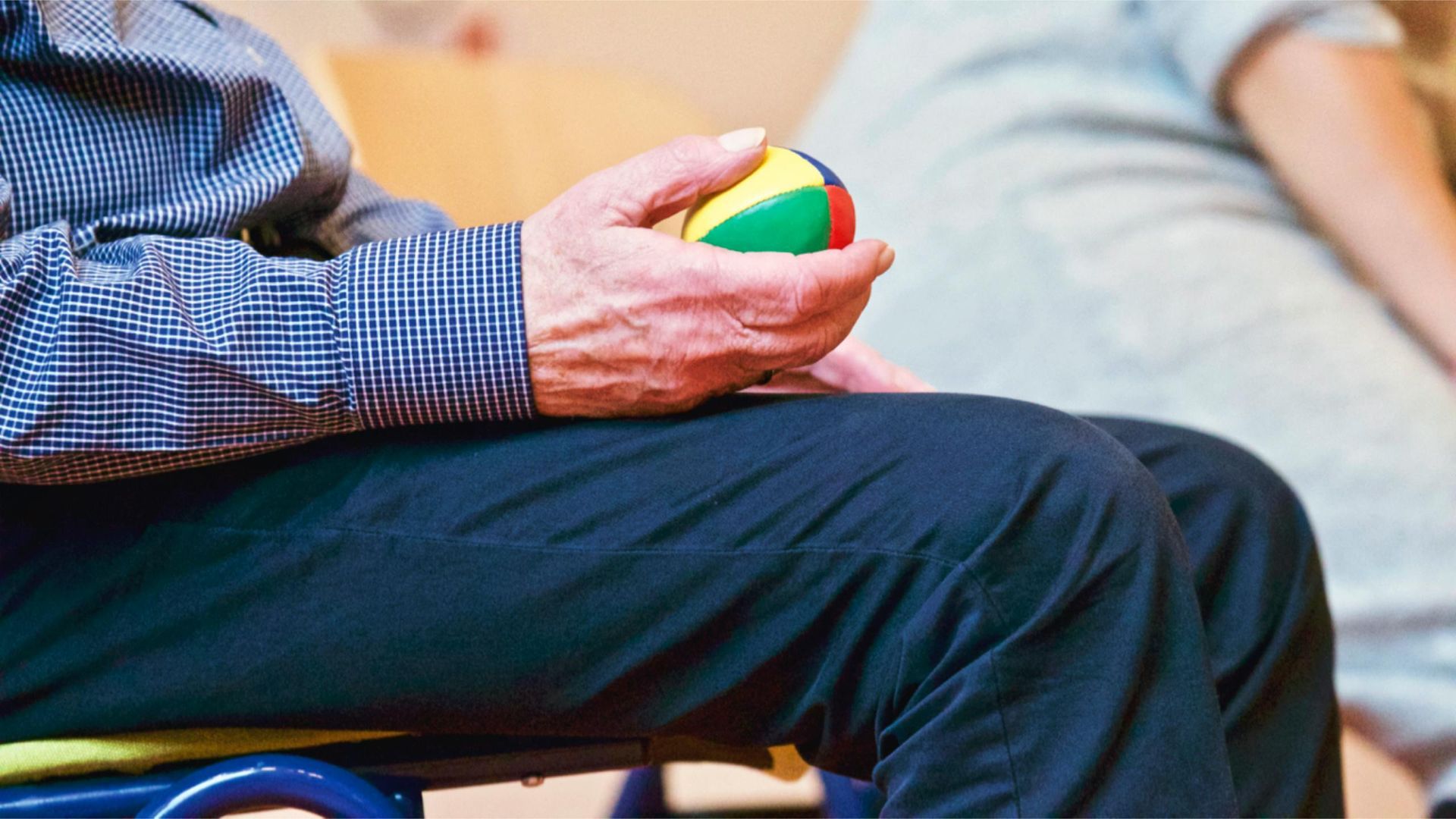 An elderly man is sitting in a chair holding a ball in his hand.