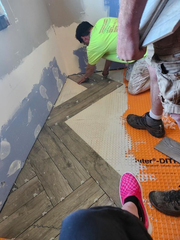 A man is laying tile on the floor in a room.