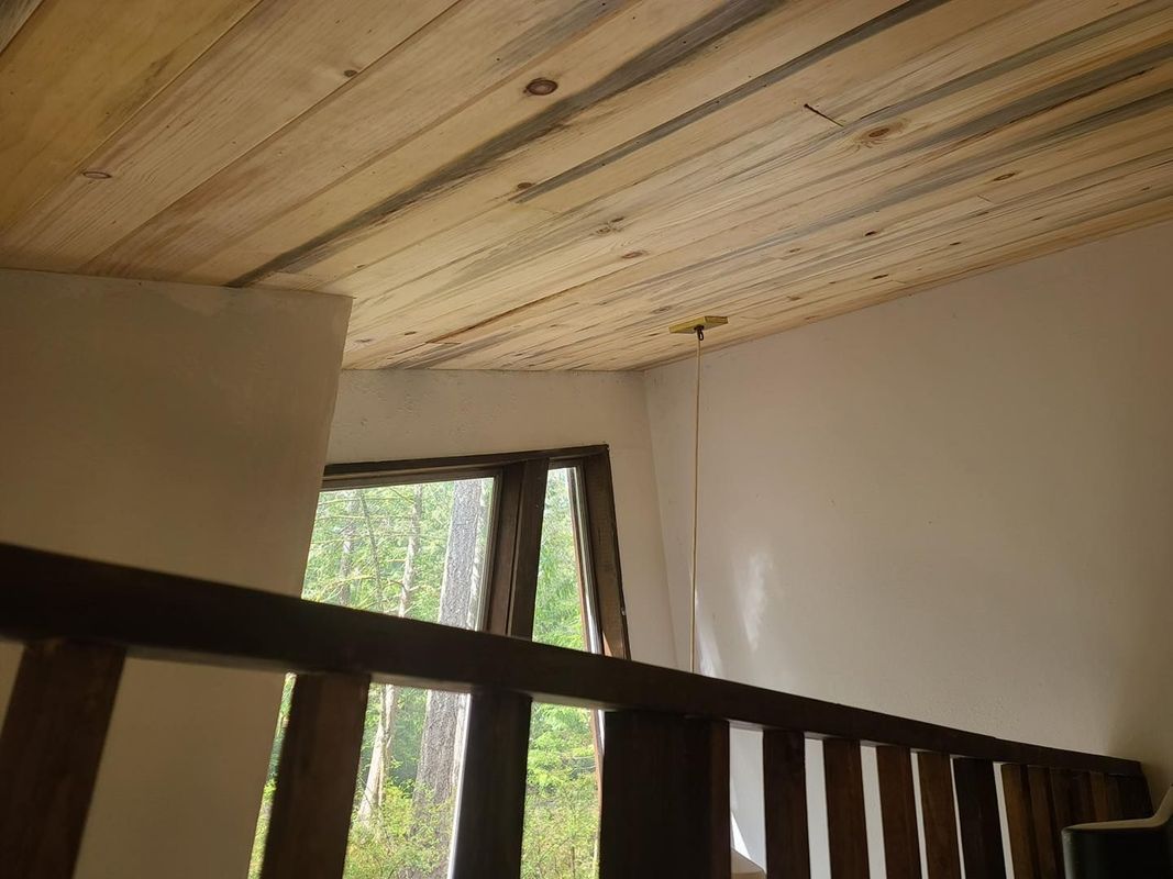 A wooden ceiling in a room with a window and stairs.