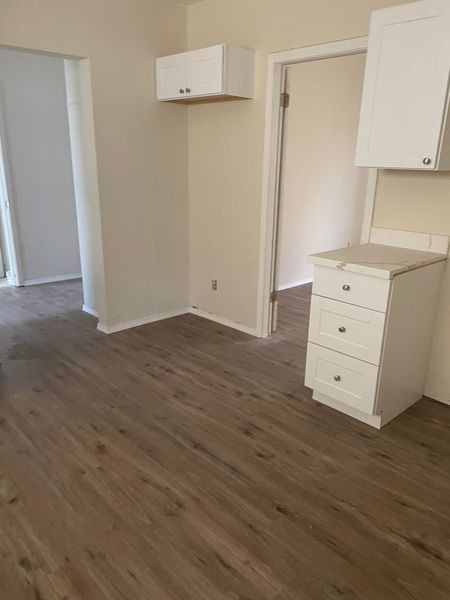 An empty room with hardwood floors and white cabinets.