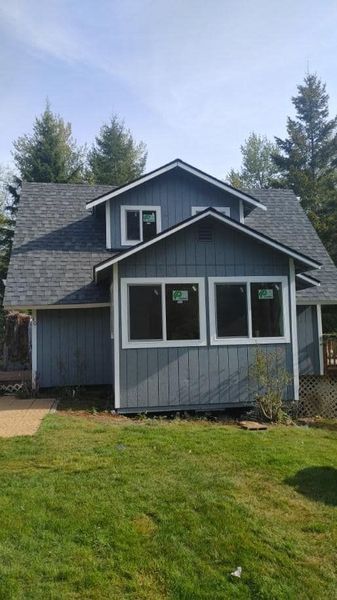 A gray house with a gray roof and white trim is sitting on top of a lush green lawn.