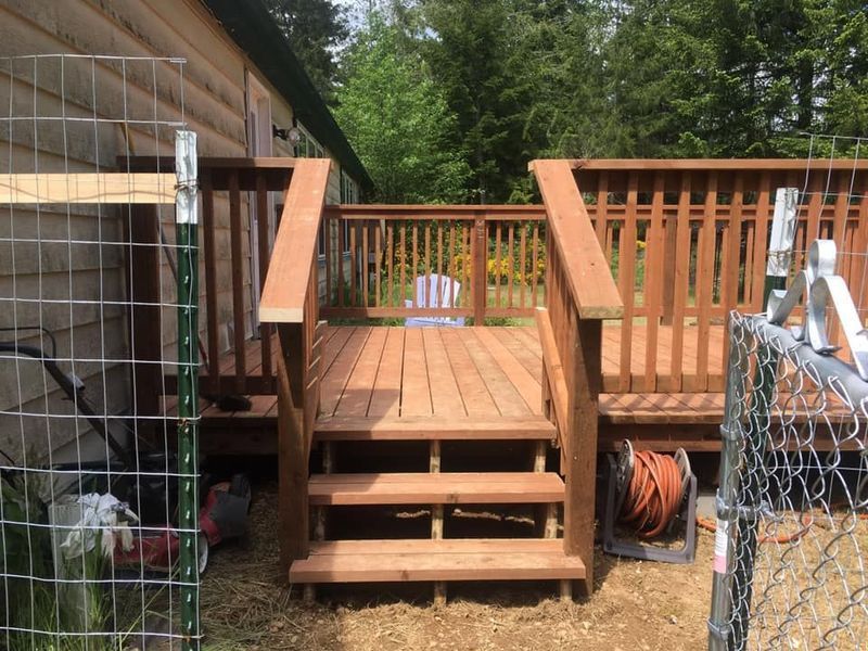A wooden deck with stairs leading up to it next to a chain link fence.