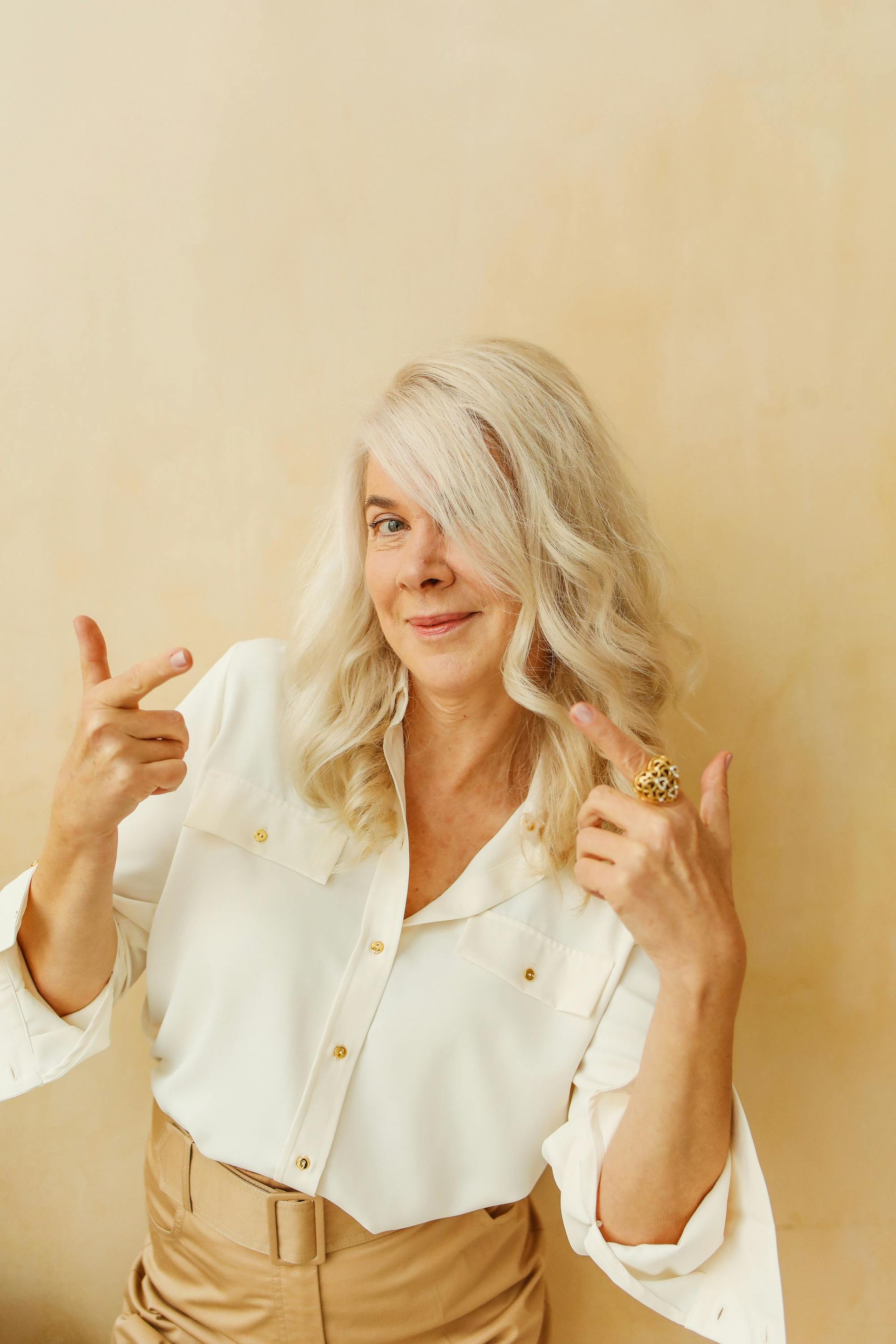 An older woman is pointing at her hair while wearing a ring.
