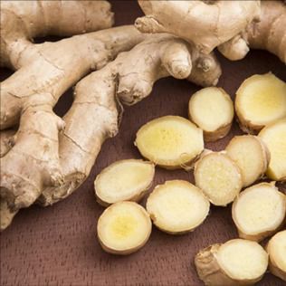 Fresh ginger root with several sliced, light-yellow rounds on a wooden surface.