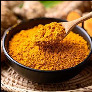 A wooden spoon scoops bright yellow turmeric powder from a dark bowl, with ginger roots blurred in the background.