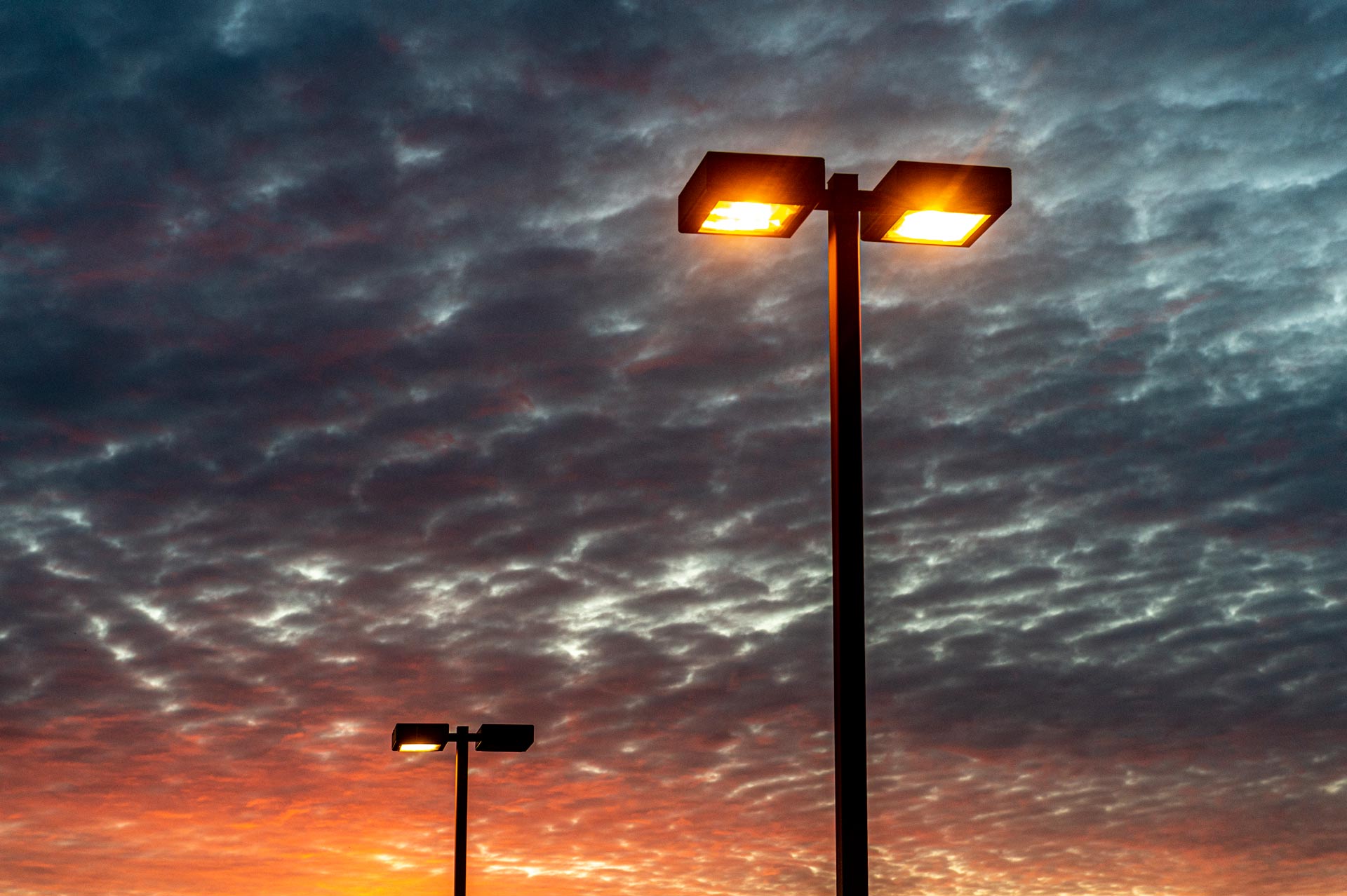 Two street lights are lit up against a cloudy sky at sunset