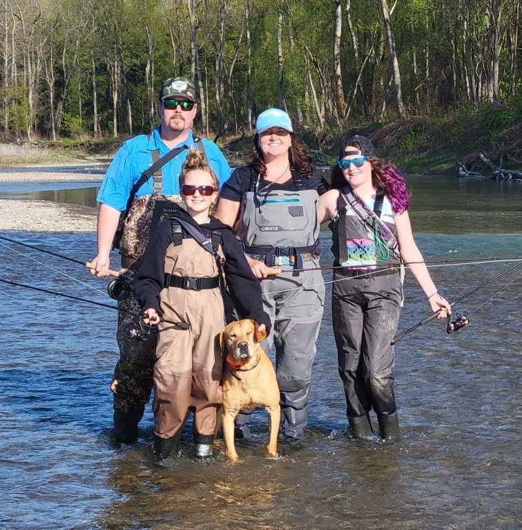 A group of people and a dog are standing in a river.