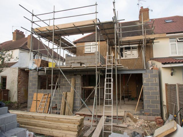 House under renovation with scaffolding, ladders, and construction materials outside.
