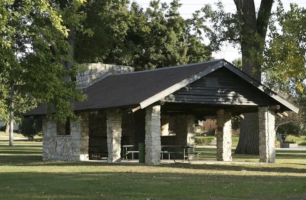 A stone pavilion with a black roof sits in the middle of a park