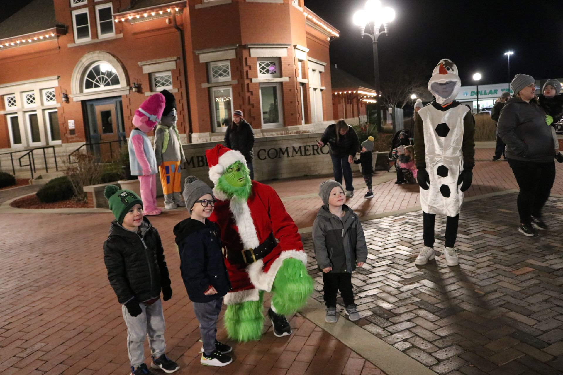 A group of children are standing next to a grinch mascot.