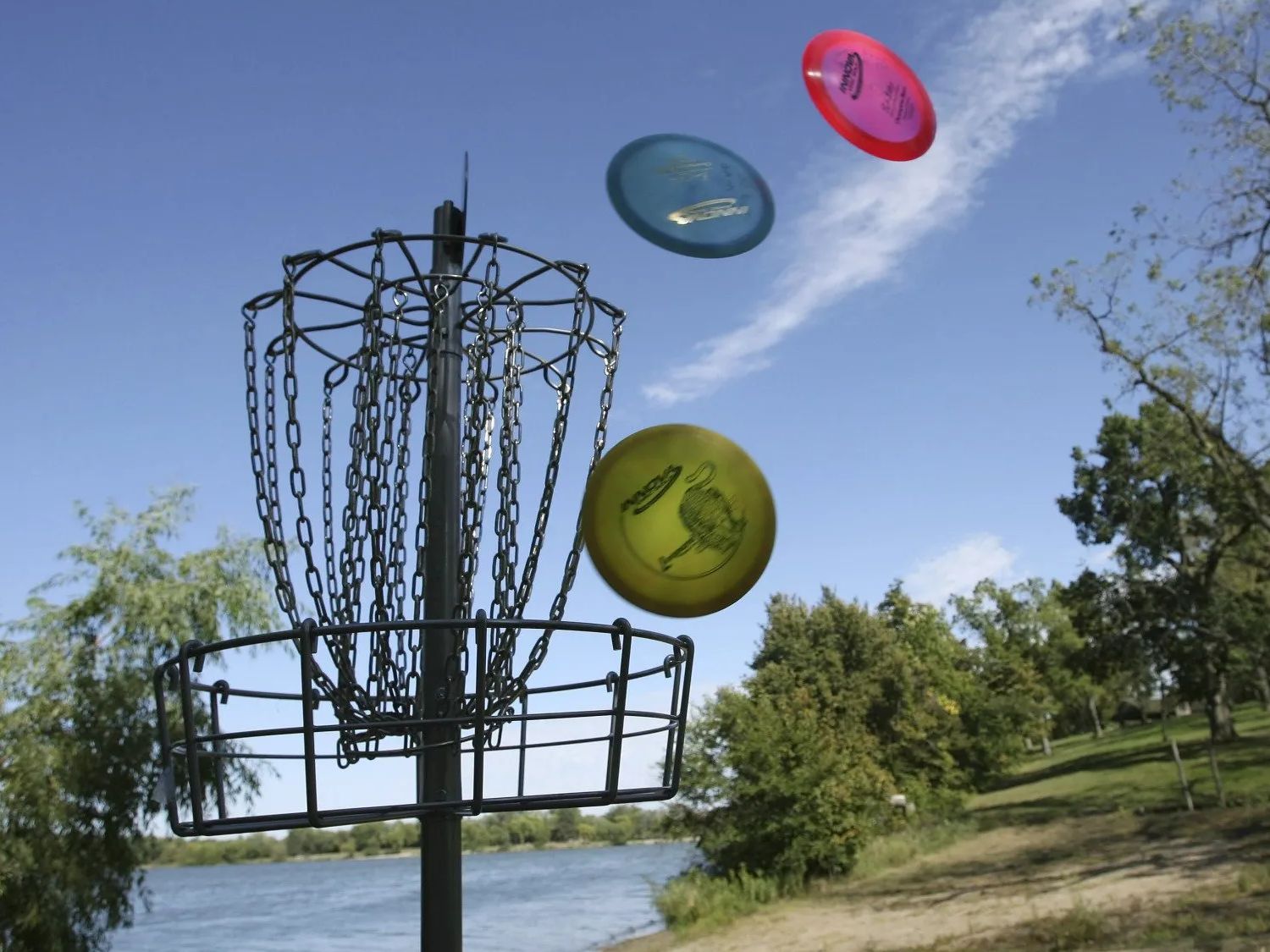 Three frisbees are flying around a disc golf basket