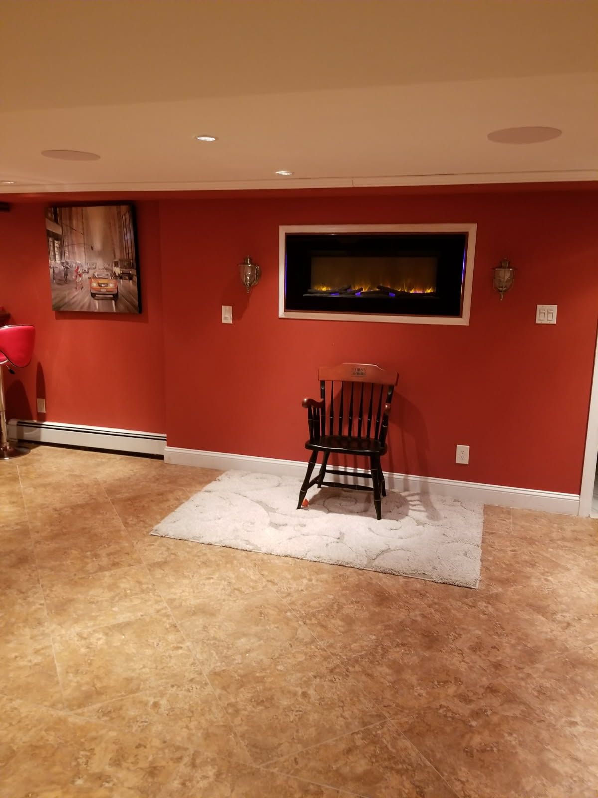 Red wall with fireplace, chair on rug, painting, and speakers in a room.