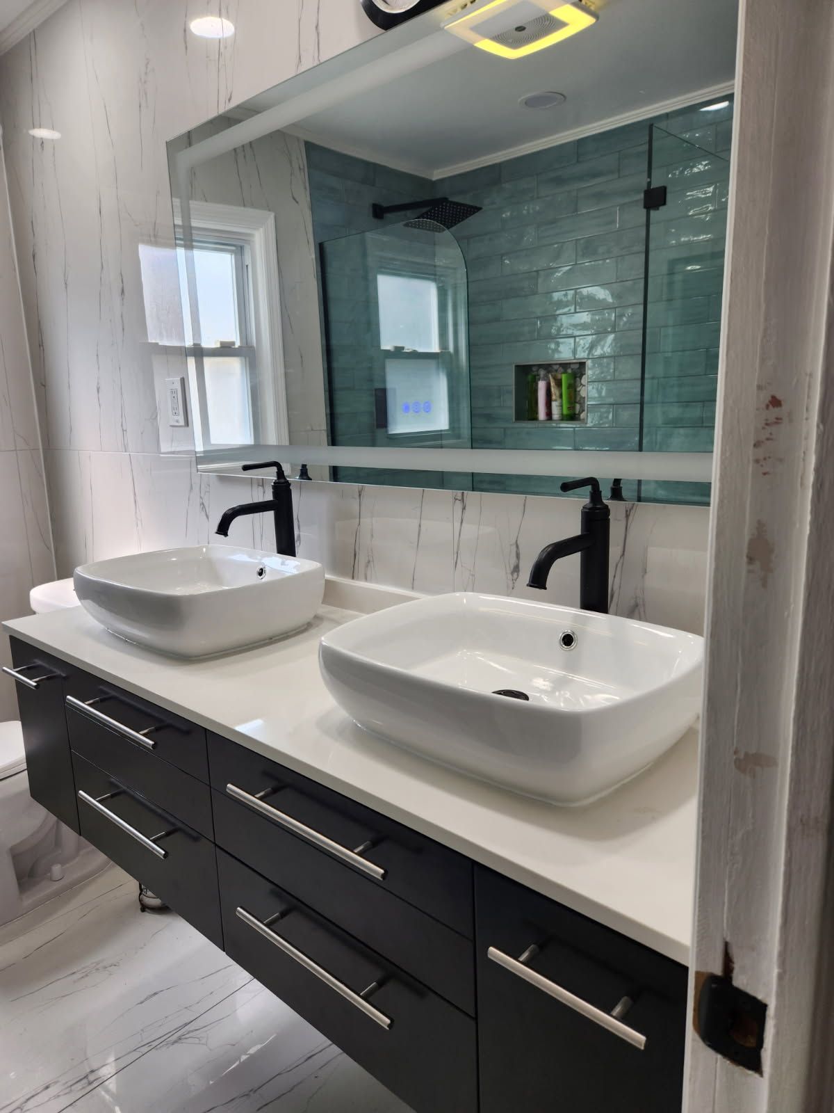 Modern bathroom with double sinks, dark cabinets, and teal shower tiling.